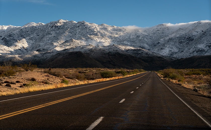 Road leading to snow-covered Weaver Mountains in Arizona under blue skies.