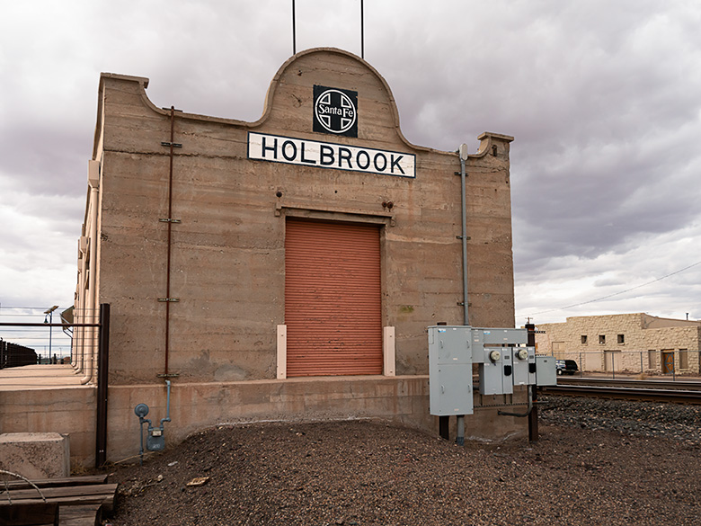 Old Holbrook train station sign with Santa Fe logo on a building repurposed as a warehouse along the railroad tracks.