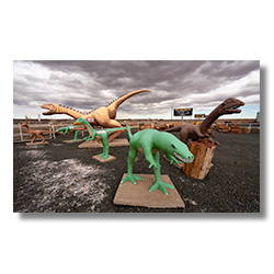 Wide-angle photo of playful dinosaur sculptures in a rock shop yard in Holbrook, Arizona, with petrified wood for sale