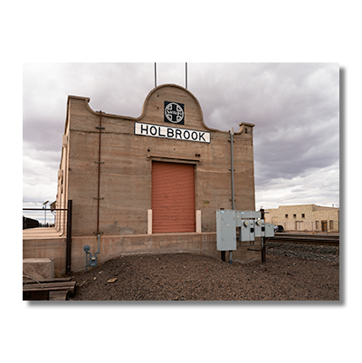 Old Holbrook train station sign with Santa Fe logo on a building repurposed as a warehouse along the railroad tracks