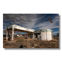 Faded green signage on an abandoned gas station under dramatic sky in Holbrook, Arizona.