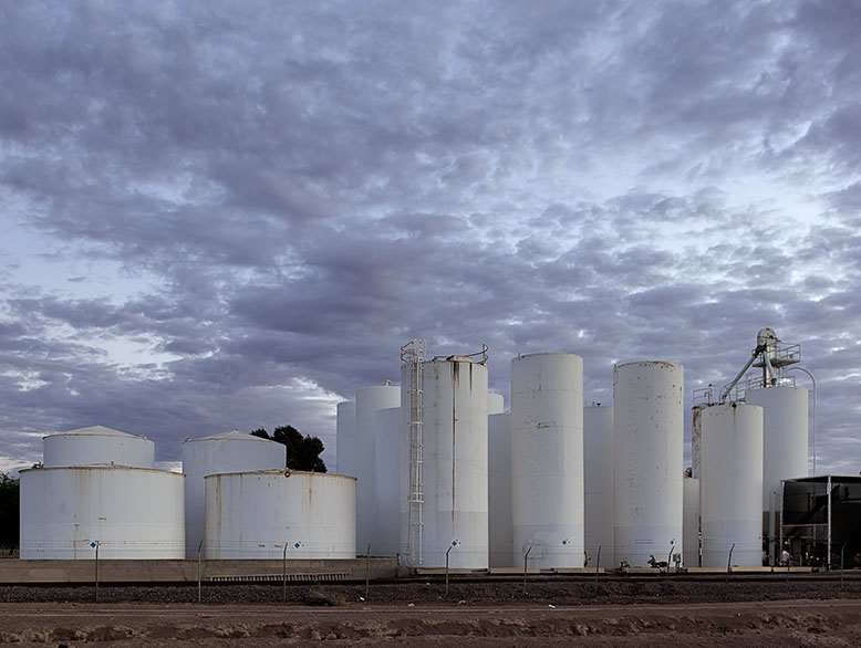 White chemical storage tanks in Buckeye, Arizona, pictured against a dramatic early morning sky with clouds overhead.