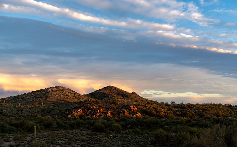 With the sun on the horizon, a rock outcrop glow red before a pair of dormant cinder cones.