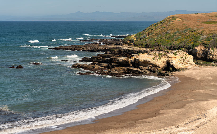 A serene view of Spooner's Cove beach and the hazy Santa Lucia Range in the distance.
