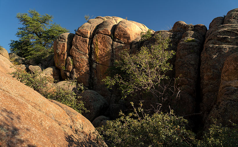 A sunlit canyon at Granite Dells with angular rock formations, highlighted by shadows and a blue sky backdrop.