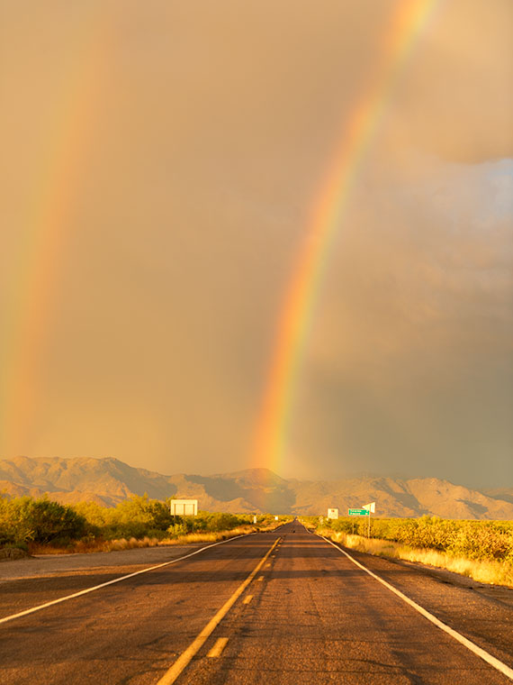 Double rainbows arching over State Route 71 with dark golden clouds and the Weaver Mountains in the background, Congress, Arizona.