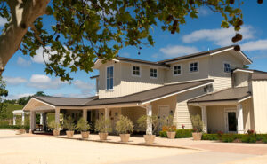 The inviting facade of Justin Winery's tasting room in Paso Robles, framed by mature oak branches and well-manicured greenery, photographed by Jim Witkowski.