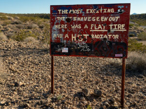 Humorous warning sign in Gold Butte, Nevada, about flat tires and hot radiators, against a desert backdrop.