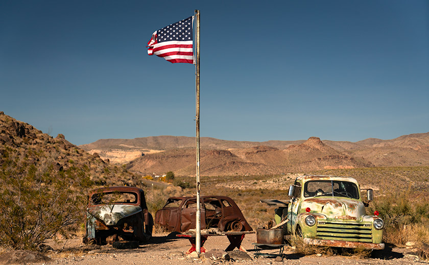 Vintage cars parked under a waving American flag at Cool Springs Station on Route 66, Oatman, Arizona.