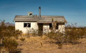 An abandoned house with broken windows, standing desolate along Route 66, symbolizing the unfulfilled dreams of past migrants.