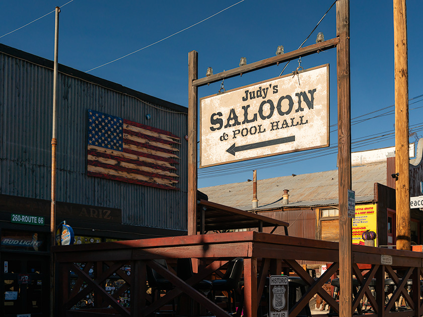 The rustic sign of Judy's Saloon and Pool Hall under a wall-mounted American flag on the historic Main Street of Oatman, Arizona.