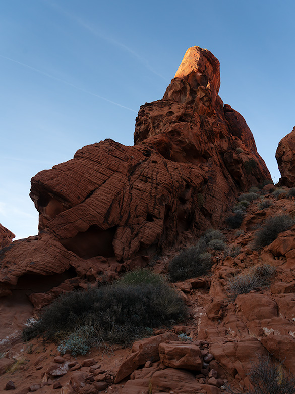 A towering red sandstone formation illuminated by the golden light of the sun, set against the clear blue sky in Valley of Fire State Park, Nevada.