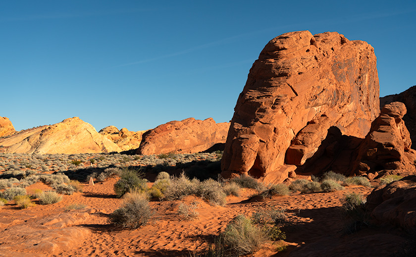 A towering red sandstone rock formation standing prominently against a clear blue sky in the Valley of Fire State Park, Nevada.