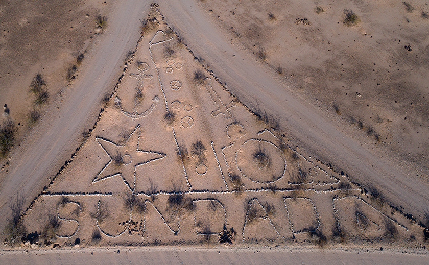 Aerial photo of triangular rock art near Sundad, Arizona, featuring an anchor, star, circles, and the word 'SUNDAD' spelled in stones