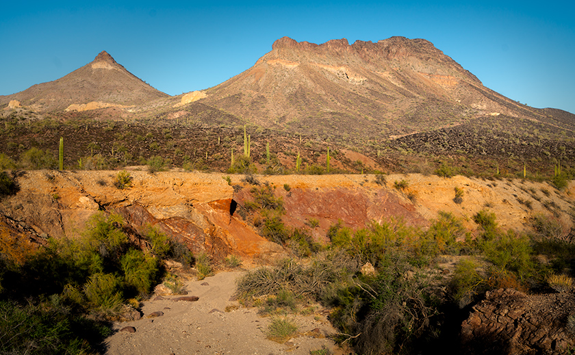Cooper Wash cutting through red rock layers with Montezuma Head and Face Mountain ridges in the Arizona desert.
