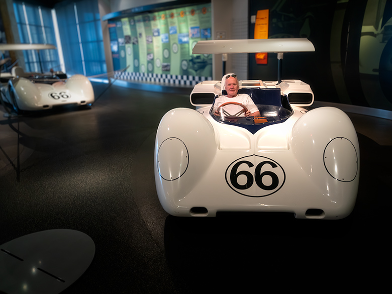 Photographer playfully sitting in a classic display car at an exhibition.