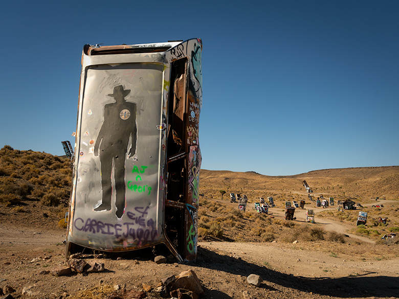 Sheriff graffiti on a car at Goldfield’s International Car Forest, surrounded by unique planted vehicles in the Nevada desert.