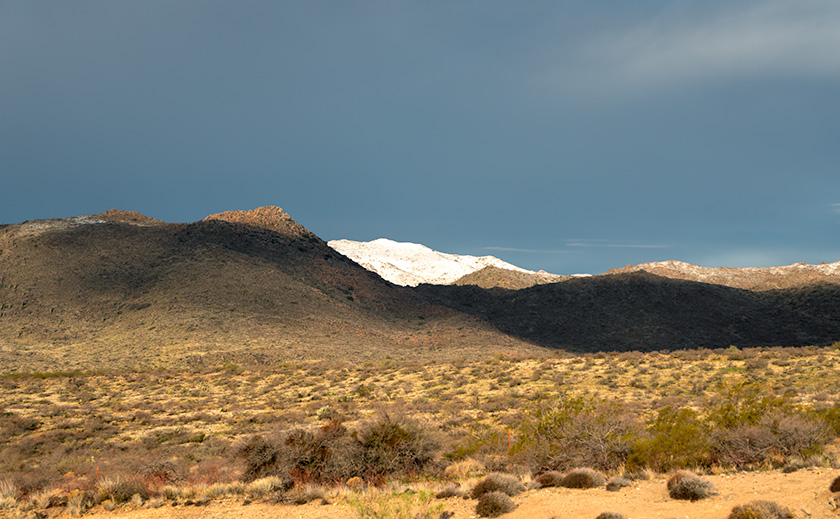 Snow-covered unnamed peak in the Date Creek Range, contrasting with dark storm clouds and the desert landscape.