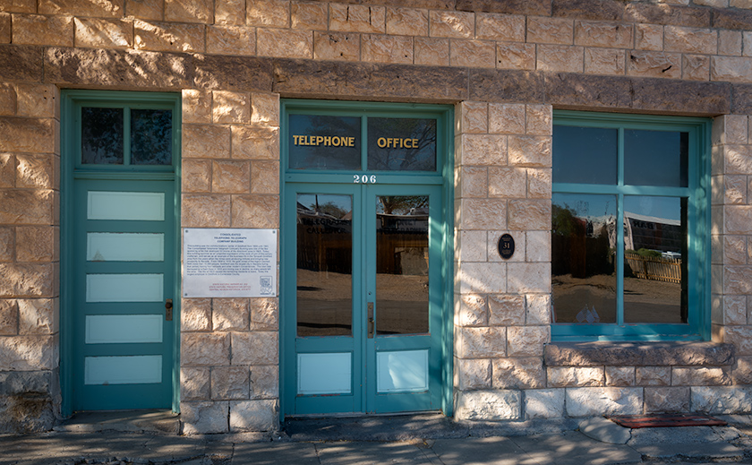 Facade of Goldfield, Nevada’s historic telephone company with aqua windows and door in bright dappled sunlight