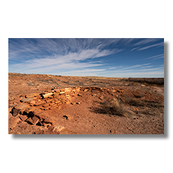 Partial wall of an ancient kiva ruin under a sweeping blue sky in Homolovi State Park, Arizona.