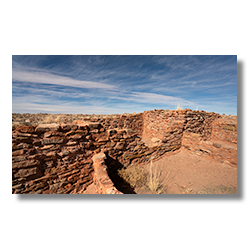 Kiva II ruins at Homolovi State Park under a wide blue sky, remnants of ancient Puebloan culture.