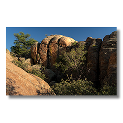 A sunlit canyon at Granite Dells with angular rock formations, highlighted by shadows and a blue sky backdrop.