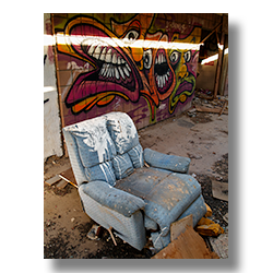  a blue reclining chair in front of a wall of graffitti by Jim Witkowski. 
