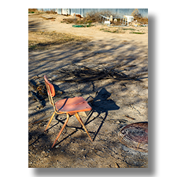 A broken school chair is used by farm hands to sit around a fire.
