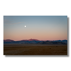 A full moon setting over the Cerbat Mountains at dawn, with pastel desert hues, captured from Route 66 near Kingman, Arizona.