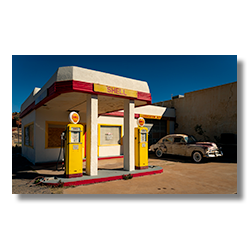 A retro Shell gas station in Layton, Arizona, with bright yellow pumps and a classic car parked nearby, framed by blue skies and mid-century architecture.